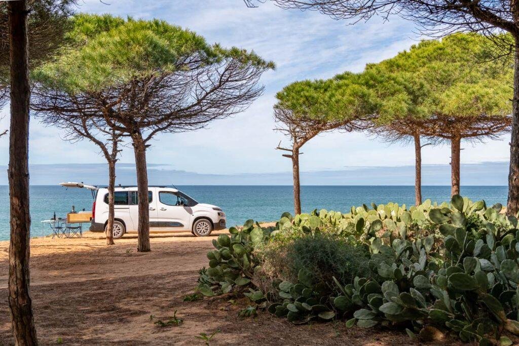 Mini campervan parked under pine trees by the sea in the Algarve