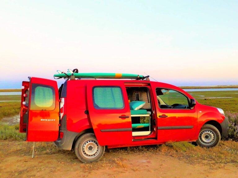 Renault Kangoo Maxi XXL mini campervan for sale in Portugal, side doors open showing the double bed, with a surfboard on the roof rails at sunset