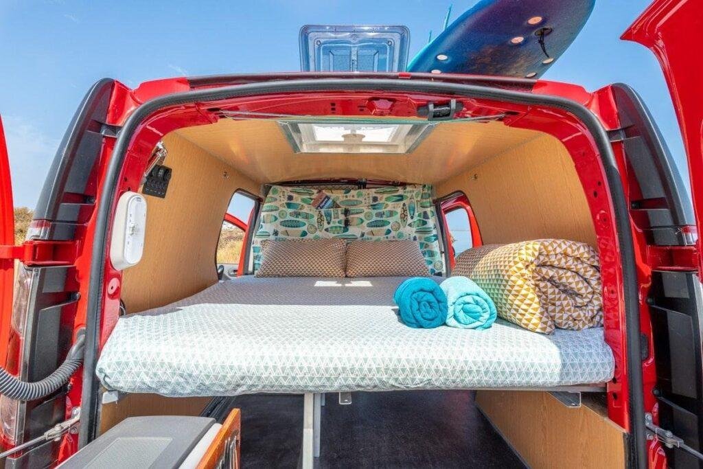 Inside a mini campervan for sale: double bed with mattress, roof window and storage underneath