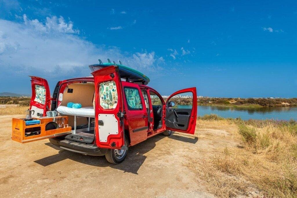 Red Renault Kangoo Maxi XXL mini campervan for sale in the Algarve, rear doors open with double bed and pull-out kitchen by the lagoon